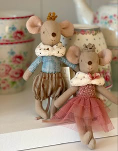 two little mice are dressed in clothes and sitting next to each other on a shelf