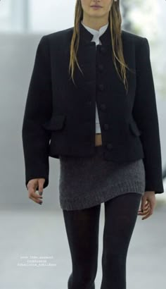 a woman walking down a runway wearing a black jacket and skirt with tights on