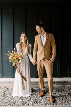 a bride and groom holding hands while standing in front of a black wall with flowers