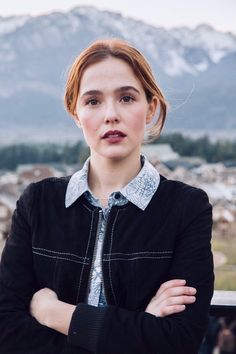 a woman standing with her arms crossed in front of mountains and snow - capped peaks