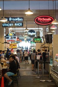 the inside of a restaurant with people sitting at tables and standing around eating food in front of neon signs