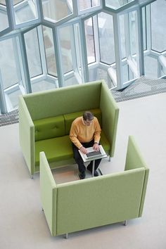 a man sitting on a green couch next to a table in a room with large windows