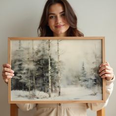 a woman holding up a painting in front of her face, with trees and snow on the ground