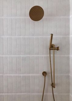 a shower head and hand held shower faucet in a white tiled bathroom with gold fixtures