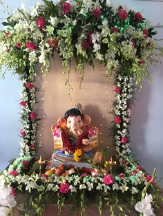 an elephant statue sitting on top of a table surrounded by flowers and greenery in front of a wall