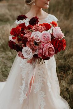 a bride holding a bouquet of red and pink flowers