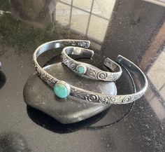 "Looking for The perfect gift for Mom and baby? This is my thickest sterling silver and turquoise cuff set.  These matching turquoise cuff sets are absolutely precious! Beautiful Kingman Turquoise and Sterling Silver adjustable floral pattern Cuff Bracelet for Mom and Baby! 8mm Kingman Turquoise for Mom with your choice cuff length and 5mm Turquoise for baby on a 4\" cuff that fits newborn to 1 year and adjustable. 💕 This .925 Sterling Silver floral pattern cuff is 5.13mm wide and 1.78mm. (Thickest set) I will hand cut, hand shape, lightly hammer, lightly oxidize, tumble for hours, set stone and hand-polish just for you! My cuffs are made to order in your size.  My Kingman turquoise is from the same batch and may vary slightly in color but are all a luscious turquoise blue.  Please see my Engraved Turquoise Sterling Silver Bracelet Gift, Stamped Turquoise Cuff Bracelet Gift, Turquoise Stamped Cuff Bracelet As Gift, Gift Turquoise Stamped Cuff Bracelet, Stamped Turquoise Bracelet As Gift, Turquoise Cuff Bracelets, Mother And Newborn, Hammered Cuff Bracelet, Mens Cuff Bracelets