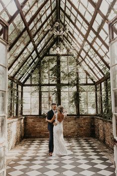 a bride and groom standing in the middle of a room with large windows, surrounded by greenery