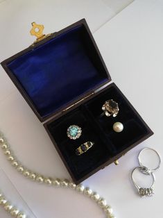 an open jewelry box with three rings and a pearl necklace on the table next to it