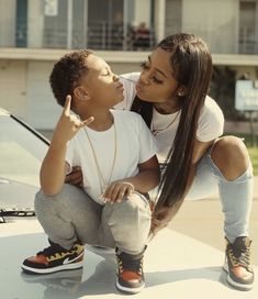 a mother and son sitting on the hood of a car, kissing each others cheek