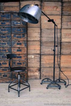 an industrial desk lamp next to a chair in front of a wall with wooden pallets