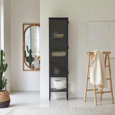 a white bathroom with a black cabinet next to a potted plant and a mirror