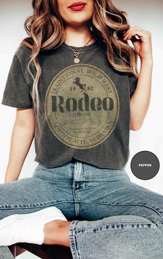 Well, howdy there, y'all! Welcome to the heart of the Wild West with our Traditional Wild West Rodeo Tee - a slice of cowboy culture that's as classic as a campfire under the stars! Let me tell ya about this tee - it's not just any ol' shirt; it's printed on genuine Comfort Colors® 1717 tees, y'all! And let me tell ya, these tees are softer than a tumbleweed rollin' through the prairie, with that vintage look and feel that'll make ya feel like you've stepped right out of a saloon from yesteryear Wild West Shirt, Vintage Crew Neck Top For Rodeo, Retro Crew Neck Tops For Western-themed Events, Retro Letter Print Tops For Rodeo, Vintage Letter Print Tops For Western-themed Events, Vintage Letter Print Tops For Rodeo, Retro Western Style Short Sleeve Top, Retro Letter Print Top For Concerts, Vintage Short Sleeve Tops For Western-themed Events