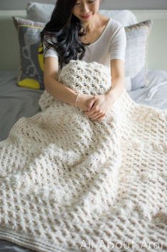 a woman sitting on top of a bed covered in a white crochet blanket