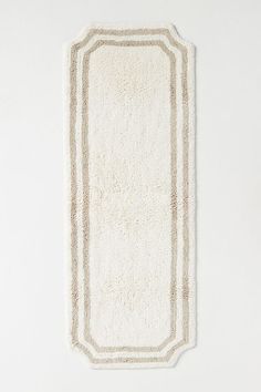 a white rug with an oval border in the middle on a white wall behind it