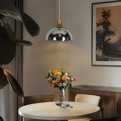 a vase with flowers sitting on top of a white table next to a chair and lamp