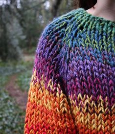 a woman wearing a multicolored knitted sweater in the woods with her back turned to the camera