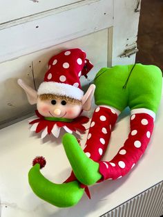 an elf doll sitting on top of a white table next to a green and red wreath