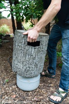 a man is holding something in his hand near a tree stump that has been turned into a trash can