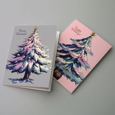 two christmas cards with watercolor trees on them, one is pink and the other is blue