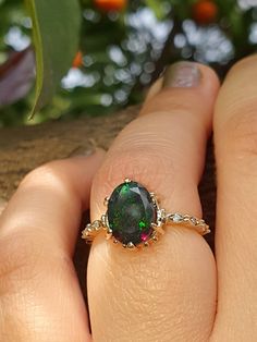 a woman's hand holding an oval shaped ring with a green and red stone