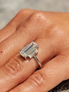 a woman's hand with a diamond ring on top of her finger and an emerald stone in the middle