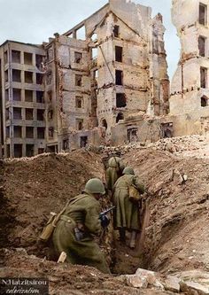 soldiers digging through trench in front of destroyed buildings