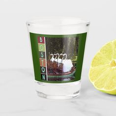 a lemon next to a shot glass with the boston swan boat on it's side