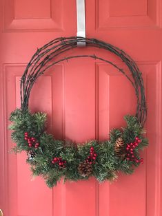 a wreath hanging on the front door with pine cones, berries and evergreens around it