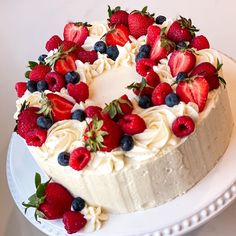 a white cake with strawberries and blueberries on top is sitting on a plate