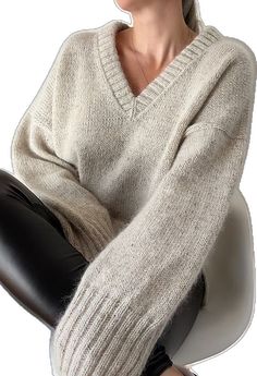 a woman sitting on top of a white chair wearing a sweater and black leggings