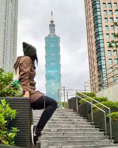 a woman sitting on the steps in front of a tall building with a sky scraper behind her