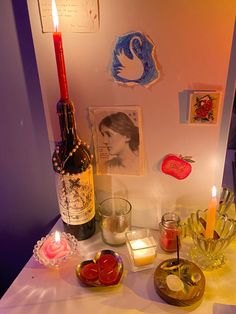 a table topped with candles and bottles of wine next to pictures on the wall behind it