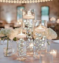 the centerpieces are filled with white flowers and floating candles in glass vases