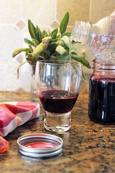 a glass of red wine sitting on top of a counter next to a jar of liquid