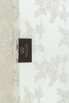 the label is on top of an ivory and white lace fabric with floral design,