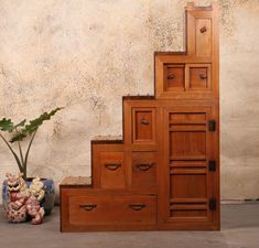 a tall wooden cabinet sitting next to a plant on top of a cement floor near a wall