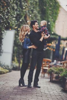 a man and woman holding a small child in their arms while standing on a brick walkway