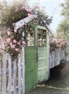 an outhouse with flowers growing over it and a wooden fence around the door that is open