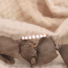 a ring with pearls on it sitting on top of a leafy plant next to a white cloth