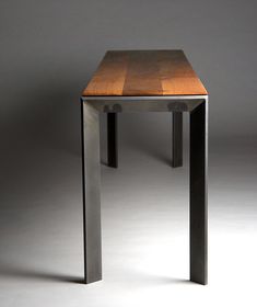 a small wooden table sitting on top of a white floor in front of a gray wall