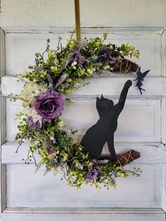 a wreath with a black cat and purple flowers hanging on the front door to decorate it