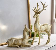 two deer figurines sitting on top of a table next to a framed mirror