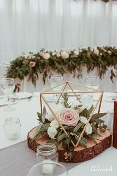 a wooden slice with flowers and greenery on it is sitting on a table in front of some candles