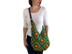 a woman wearing a white shirt holding a green and orange crocheted bag with an orange flower on it