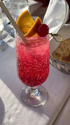 a glass filled with liquid sitting on top of a table next to bread and wine glasses