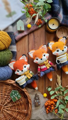 three knitted foxes sitting on top of a wooden table next to yarn balls and oranges