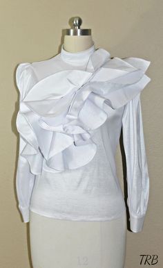 Add a high fashion statement to your wardrobe with this tiered asymmetrical ruffled Blouse. If you love being unique and the center of attention, this blouse will defiantly have all eyes on you! The low cut turtleneck neckline adds a soft, feminine touch and others will defiantly be impressed with your fashion sense. The cascade of asymmetrical ruffles across the front gives the blouse a unique wow factor. The blouse has a tailor fit and is very comfortable to wear. Made of 100% Taffeta, light w Feminine Party Tops With Ruffles, Elegant Party Tops With Ruffles, Elegant Ruffled Tops For Party, Chic Fitted Blouse With Ruffles, Chic Fitted Ruffle Blouse, Fitted Ruffle Hem Blouse For Party, Fitted Blouse With Ruffle Hem For Party, Fitted Tops With Ruffled Collar For Party, Fitted Party Tops With Ruffled Collar