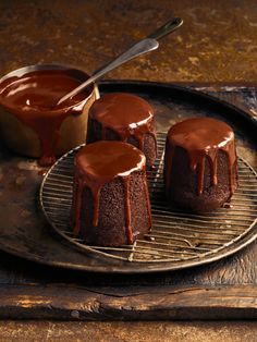 three cakes with chocolate icing on a cooling rack, one being drizzled with caramel