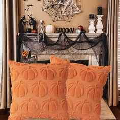 two orange pillows sitting on top of a bed in front of a fireplace with halloween decorations